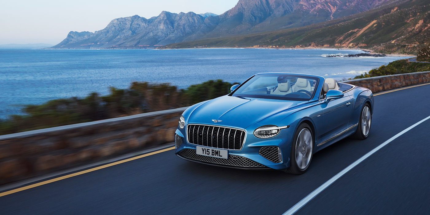 Bentley Cyprus New Bentley Continental GTC Azure convertible in Light Windsor blue paint with 22 inch Azure wheels and chrome grill, driving dynamically by the sea