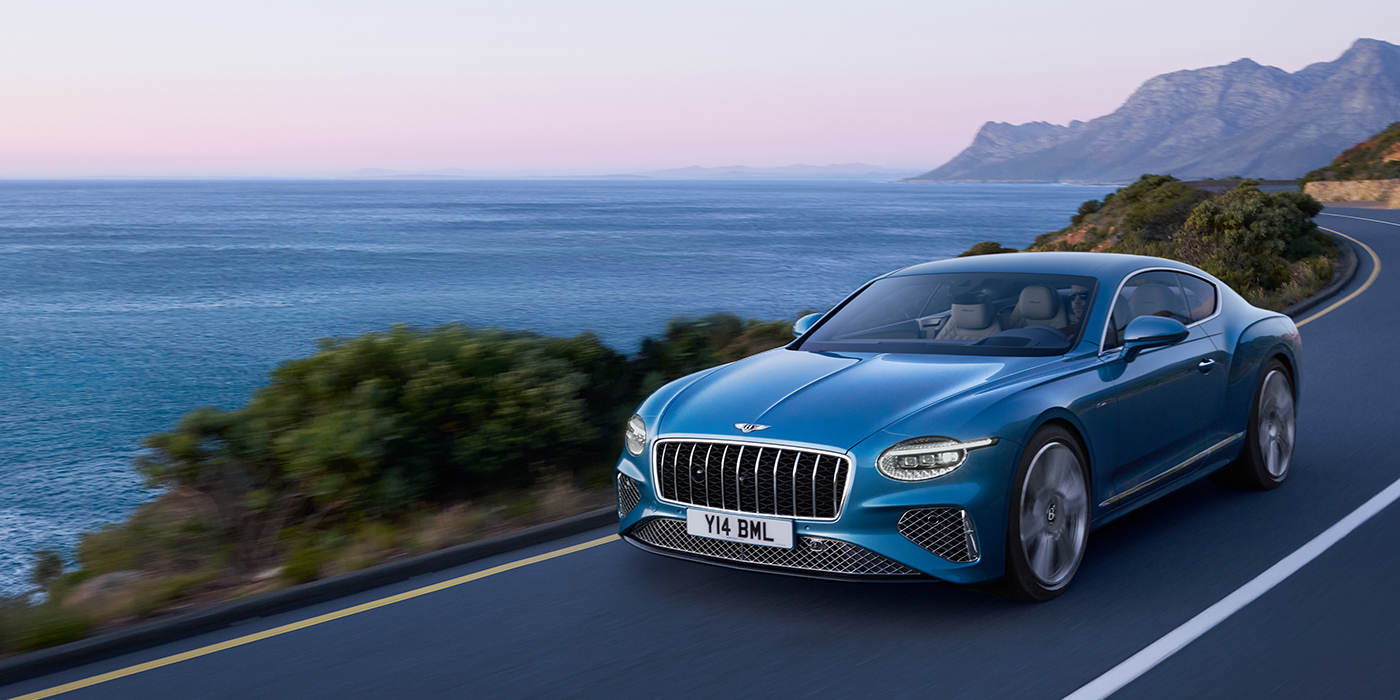 Bentley Cyprus New Bentley Continental GT Azure coupe in Light Windsor blue paint with 22 inch Azure wheels and chrome grill, driving dynamically by the sea