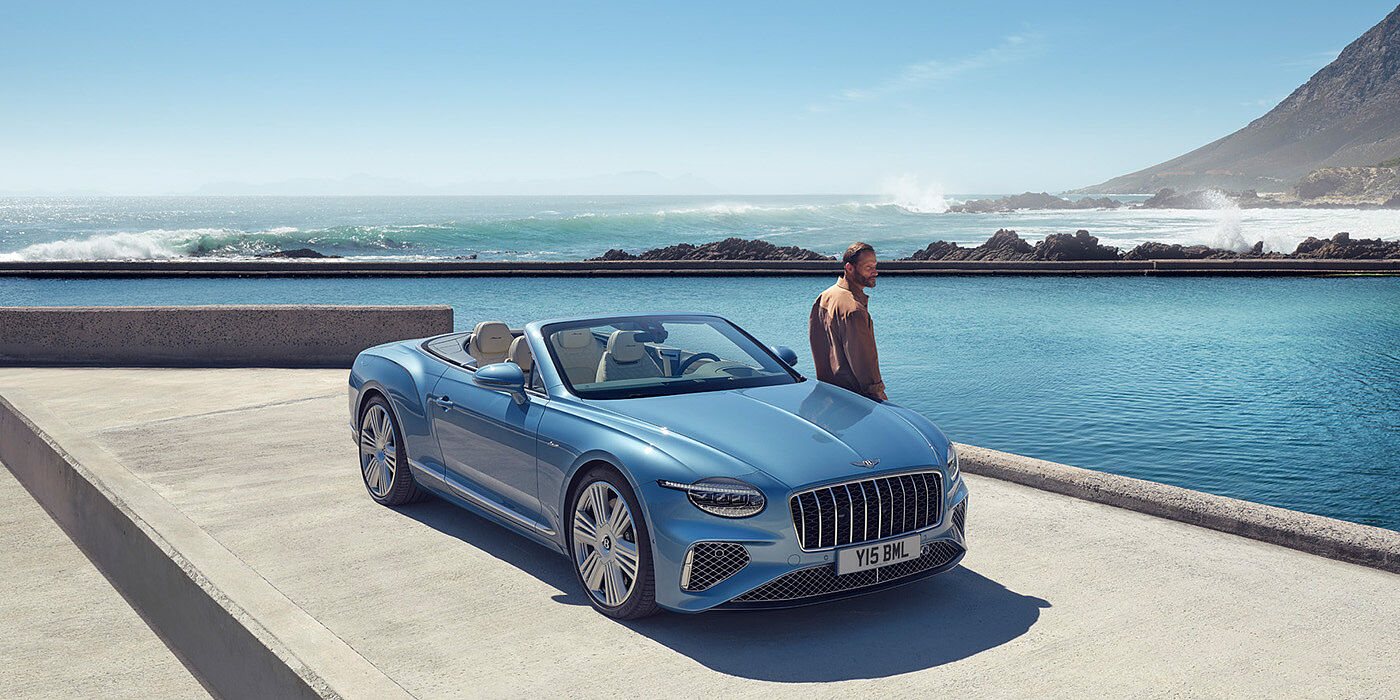 Bentley Cyprus New Bentley Continental GTC Azure convertible front view in Light Windsor blue paint with 22 inch ten spoke wheels parked by the sea in the sunshine