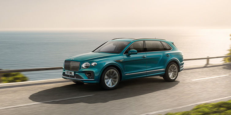 Bentley Cyprus Bentley Bentayga Extended Wheelbase Azure SUV in Topaz blue paint driving dynamically by the ocean